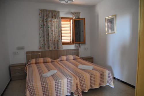 Habitación en el hostal Pension Eva de Puerto de Mogán con cama doble, muebles de madera y cortinas florales