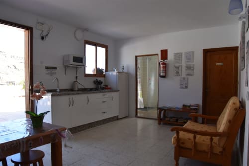 Área común del hostel Pension Eva en Puerto de Mogán con cocina, muebles de madera y ventanas luminosas