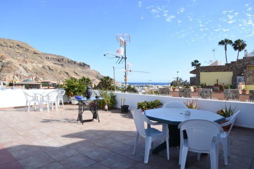 Terraza de la azotea del hostal Pension Eva en Puerto de Mogán con mobiliario blanco, vistas al mar y palmeras