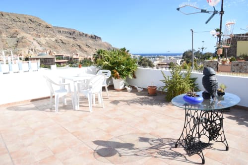 Terraza en la azotea de la pensión Eva en Puerto de Mogán con vistas al mar, muebles blancos y plantas en macetas
