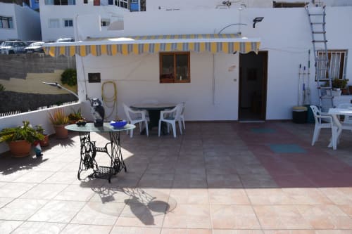 Terraza en la azotea del hostal Pension Eva en Puerto de Mogán con toldo de rayas, muebles blancos y macetas