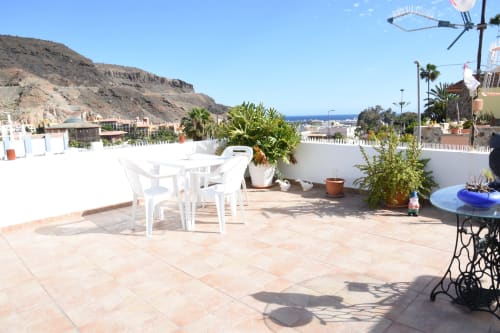 Terraza en la azotea de la pensión Eva en Puerto de Mogán con muebles blancos, vistas al mar y plantas en macetas