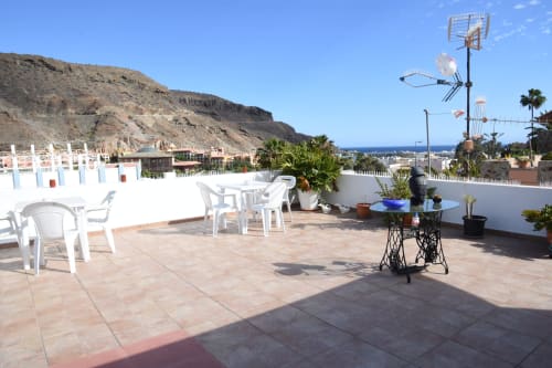 Terraza en la azotea de la pensión Eva en Puerto de Mogán con muebles blancos, vistas al mar y paisaje de montañas costeras