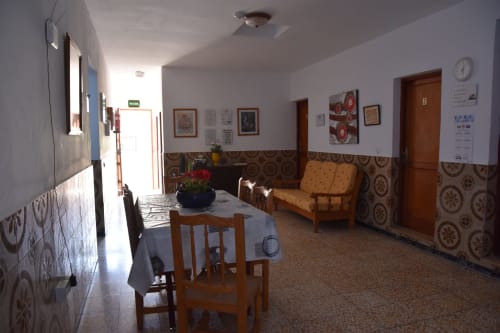 Sala común de la pensión Eva en Puerto de Mogán con mesa de comedor, muebles de madera y azulejos decorativos en las paredes