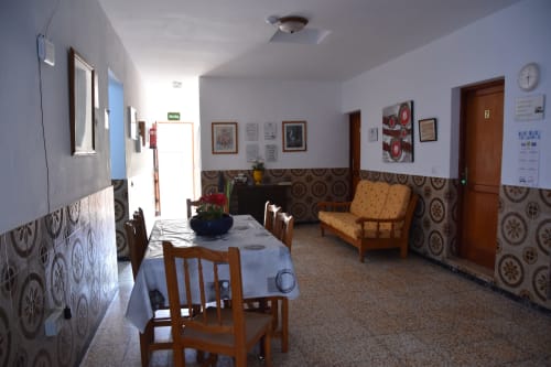 Sala común del hostal Pension Eva en Puerto de Mogán con mesa de comedor, sillas de madera, sofá y paredes con azulejos de patrón decorativo