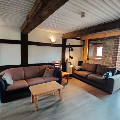 Spacieuse salle de séjour à La Ferme De Werpin avec poutres apparentes, sièges confortables, table en bois et cheminée en brique