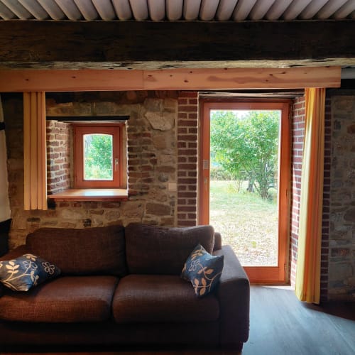 Rustic brick interior with brown sofa, large windows, and garden access at La Ferme De Werpin