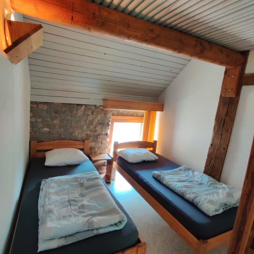 Cozy bedroom with two single beds, wooden beams, stone wall, and bright window at La Ferme De Werpin, Hotton