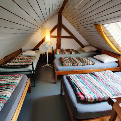 Spacious attic bedroom with multiple beds, wooden beams, and colorful striped bedding at La Ferme De Werpin BnB in Hotton