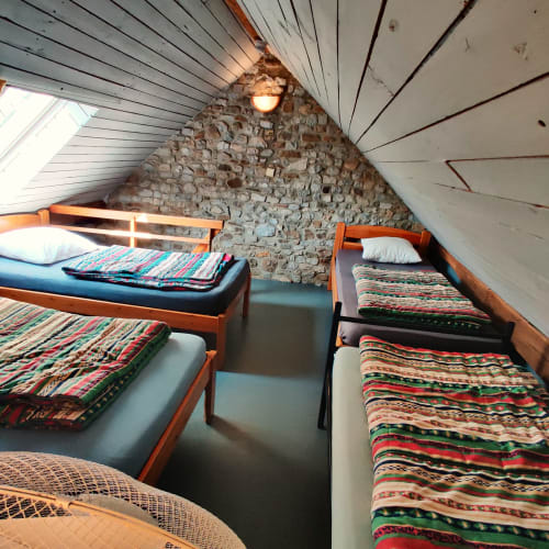 Cozy attic bedroom in La Ferme De Werpin B&B with exposed stone wall, sloped ceilings, wooden beds, and colorful woven
