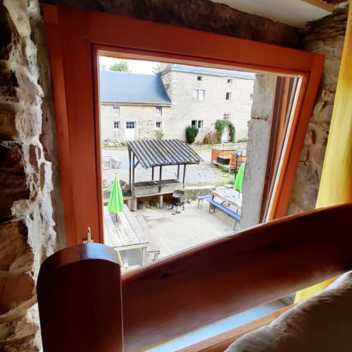 View from La Ferme De Werpin apartment window overlooking courtyard with striped awning, green umbrellas, and stone buildings