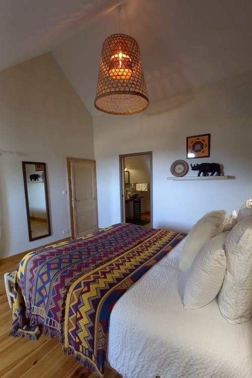 Chambre spacieuse à La Maison De Fleurat avec luminaire suspendu tressé, couvre-lit motifs et portes donnant sur le jardin