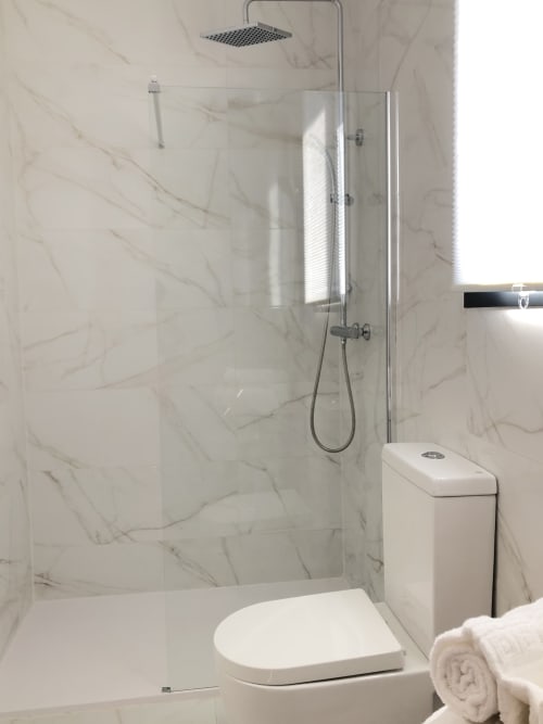 Baño moderno en Cabañas Compostela con ducha de mármol, inodoro blanco y alcachofa de lluvia en Santiago de