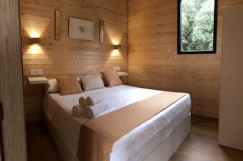 Acogedor dormitorio de cabaña de madera en Cabañas Compostela con cama queen, iluminación cálida y ventana con vista al jardín en Santiago de