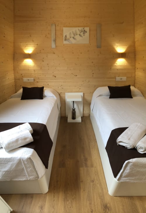 Dos camas individuales con sábanas blancas en moderna cabaña de madera en Cabañas Compostela, Santiago de Compostela