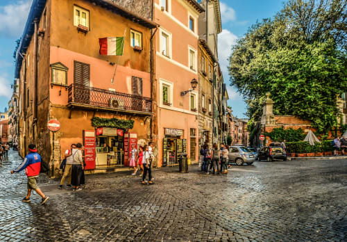 Charming cobblestone Rome street with ochre buildings, Italian flag, and local cafes near Maison Vaticana Guest House