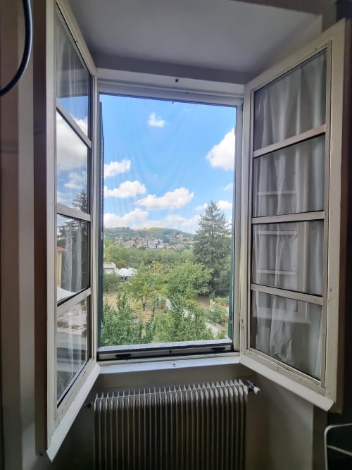 Finestra aperta del B&B La Corte Ovada con vista sul giardino, fiume, alberi e collina a Ovada, Italia