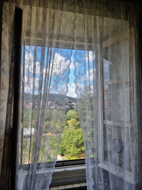 Tende di pizzo incorniciano la vista sul giardino dalla camera di B&B La Corte Ovada a Ovada, Italia, mostrando un paesaggio verde