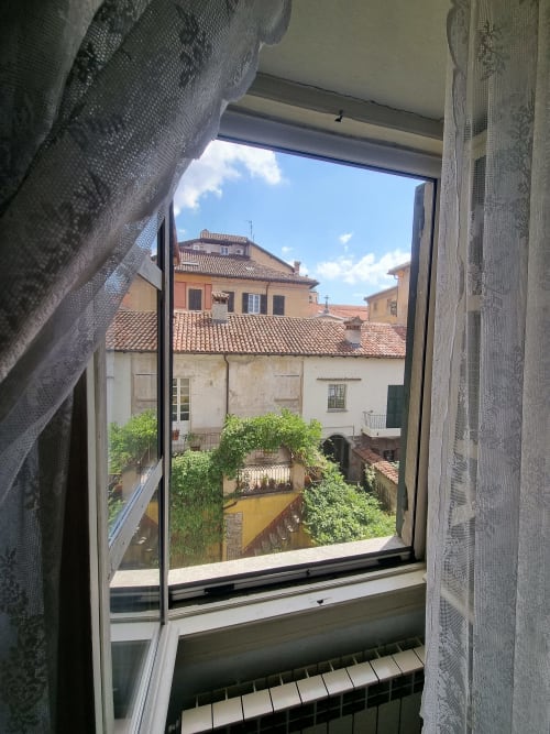 Vista dalla finestra del cortile storico con edera, tetti in cotto e edifici tradizionali a La Corte Ovada a Ovada, Italia