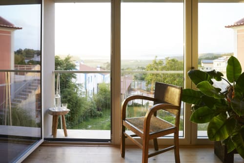 Balcony room at Cavalo de Madeira guesthouse in Arelho with sea view, wooden chair, potted plant, and countryside landscape