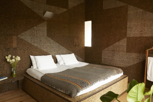 Modern bedroom at Cavalo de Madeira in Arelho with cork walls, white pillows, and natural light from skylight window