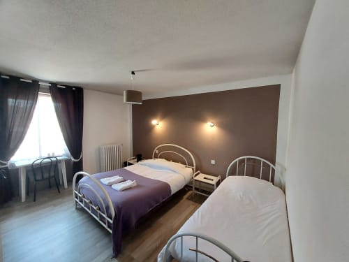 Chambre du Comtois BnB à Saône avec deux lits, mur d'accent marron, luminaire suspendu et fenêtre aux rideaux foncés