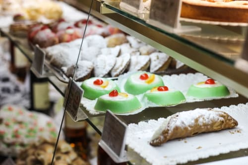 Esposizione di dolci e pasticcini siciliani presso la pasticceria Sicilianinsta Rooms a Catania, con torte dai topping verde e ricoperte di zucchero