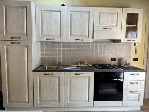 Cucina moderna con ante color crema, piano di lavoro nero, fornello a gas e lavello nello Studio Apartment di Residence La Corte, Vezza