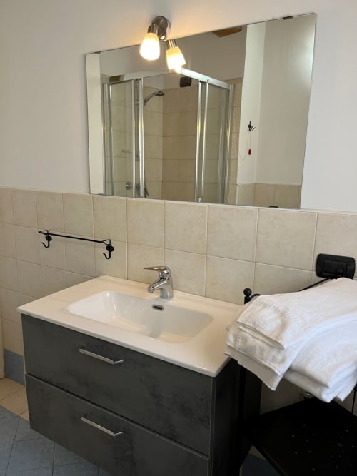 Bagno moderno con vanity scura, lavabo bianco, specchio grande e pareti piastrellate a Residence La Corte a Vezza d'Oglio