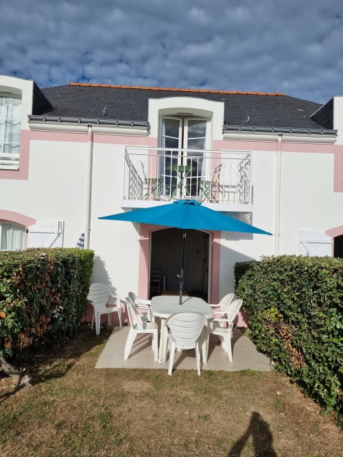 Appartement moderne Locations Loc'Maria à Belle Île en Mer avec parasol bleu, mobilier de patio blanc et balcon vue mer.