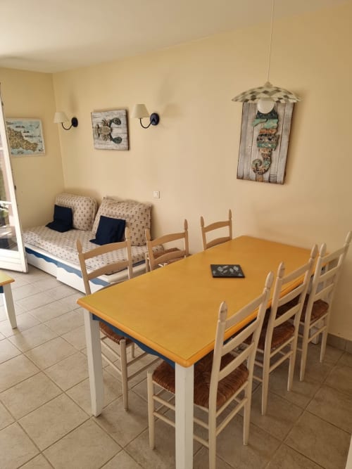 Salle à manger lumineuse avec table jaune, chaises en bois et canapé dans cette location de vacances à Belle île en mer