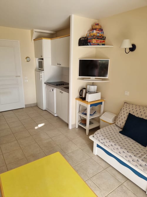 Studio à Belle-Île-en-Mer avec kitchenette, lit, TV et tapis de yoga jaune sur carrelage