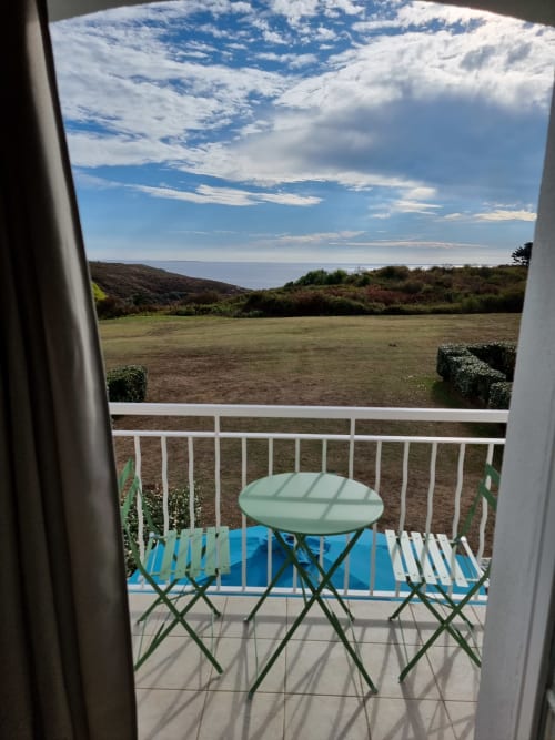 Vue du balcon de l'appartement Locations Loc'Maria avec table et chaises surplombant la prairie et la mer, Belle Île en Mer