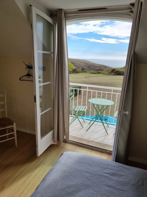 Chambre avec portes vitrées ouvertes sur balcon vue sur les champs verts et collines à Locmaria, Belle Île en Mer