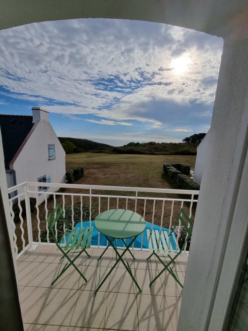 Balcon d'appartement côtier avec table et chaises vertes surplombant les champs et la mer à Locmaria, Belle Île en Mer