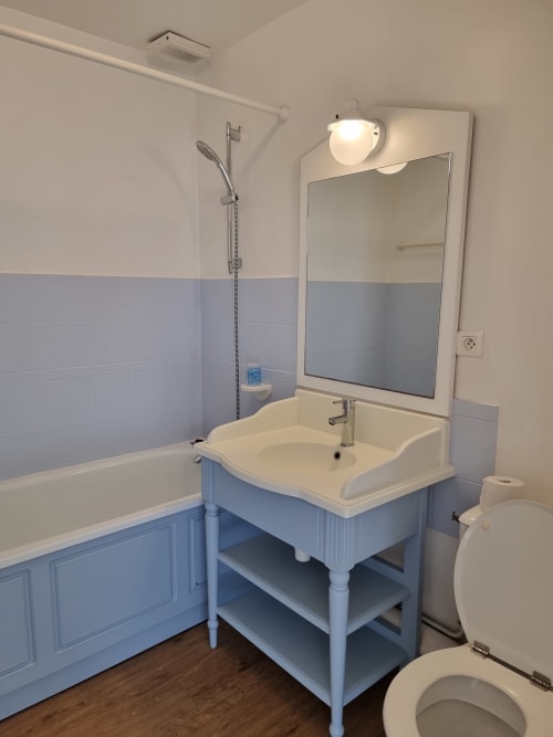Salle de bain moderne de l'appartement Locmaria avec vanité bleue, lavabo blanc, miroir éclairant, baignoire et toilettes
