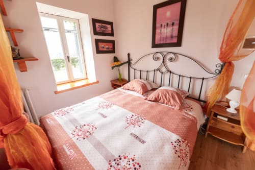 Camera luminosa a Il Podere Prato con letto in ferro battuto ornamentale, biancheria rosa, tende arancioni e quadri incorniciati a Predappio Alta.