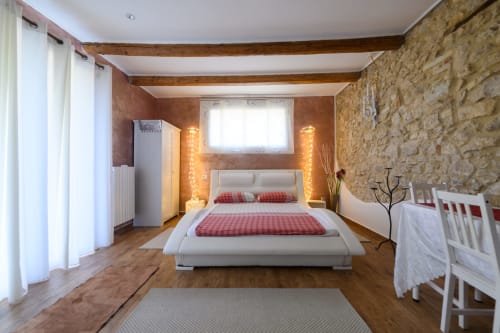 Camera moderna dell'appartamento Il Podere Prato a Predappio Alta con letto bianco, muri in pietra, travi in legno e illuminazione calda.