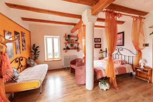 Camera luminosa a Il Podere Prato con travi a vista, accenti in terracotta, letto a baldacchino e tende ariose arancioni a Predappio