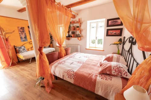 Camera da letto spaziosa a Il Podere Prato con letto a baldacchino, tende arancioni e pavimenti in legno rustico a Predappio Alta