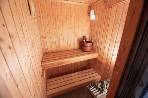 Interno di sauna in legno con panche a gradini e secchio tradizionale all'hotel Il Podere Prato a Predappio Alta, Italia