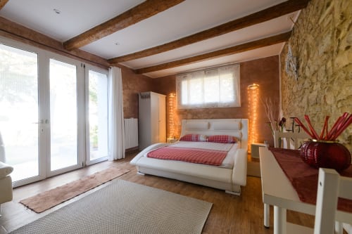 Camera da letto spaziosa a Il Podere Prato con letto bianco, travi in legno, muri in pietra e porte in vetro che si aprono sul giardino