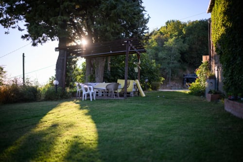 Terrazza rustica del giardino a Il Podere Prato a Predappio Alta con pergolato, sedute e alberi maestosi al tramonto