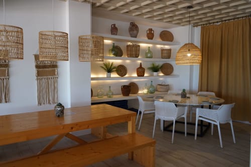Modern dining area at Hotel Sa Roqueta in Can Picafort with woven pendant lights, wooden tables, and decorative shelving.
