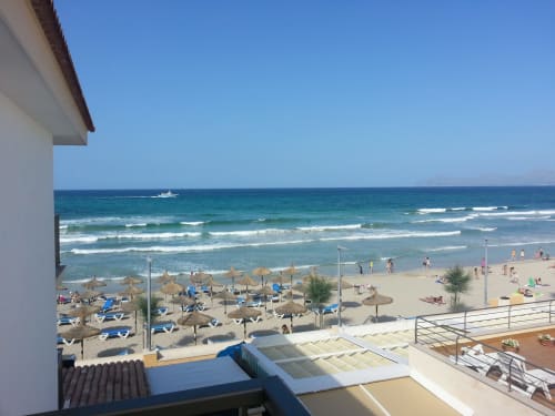 Hotel Sa Roqueta balcony view of Can Picafort beach with umbrellas, sand, and Mediterranean Sea waves