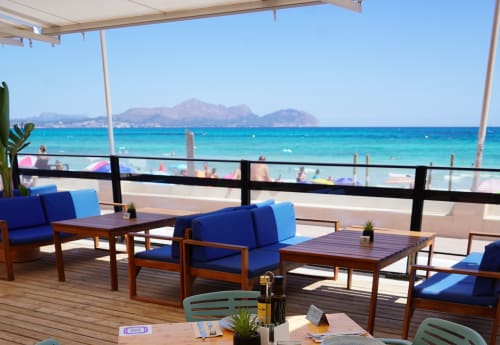 Hotel Sa Roqueta beachfront terrace in Can Picafort with blue cushioned seating, turquoise sea, and mountain views