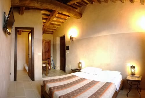 Camera matrimoniale rustica a Casale di Poggioferro con travi in legno, biancheria bianca e illuminazione calda