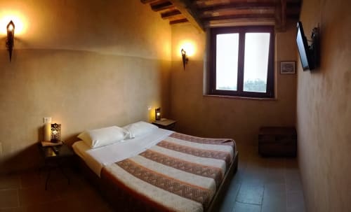Camera da letto rustica e accogliente a Casale di Poggioferro con letto matrimoniale, muri in terracotta, travi in legno e ampia finestra con vista