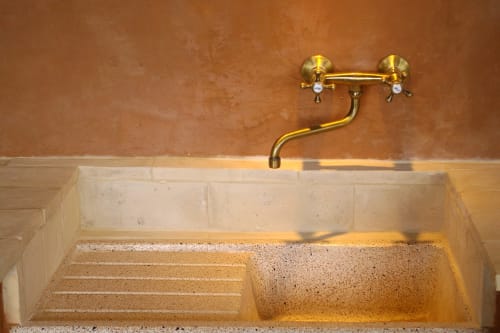 Rubinetto in ottone a parete sopra lavandino in cemento rustico nell'appartamento Casale di Poggioferro, Toscana