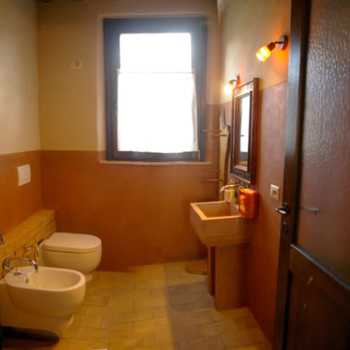 Bagno di Casale di Poggioferro con pareti in terracotta, lavabo in legno, toilette, bidet e finestra